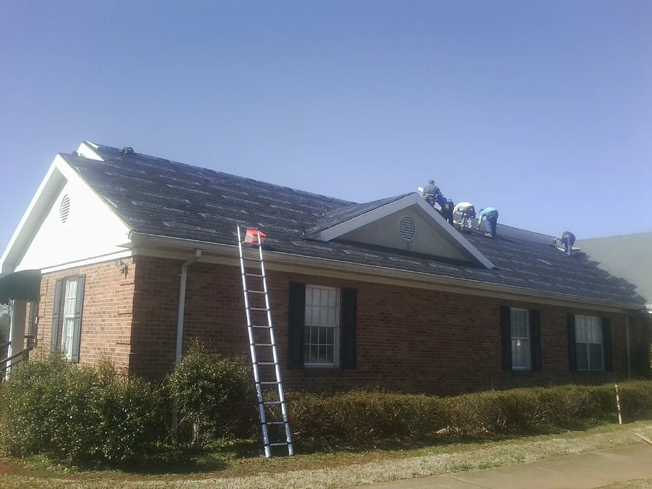 Crew tearing shingles off a brick ranch roof with a ladder set — Emergency Roof Repair work by our crew in Chualar