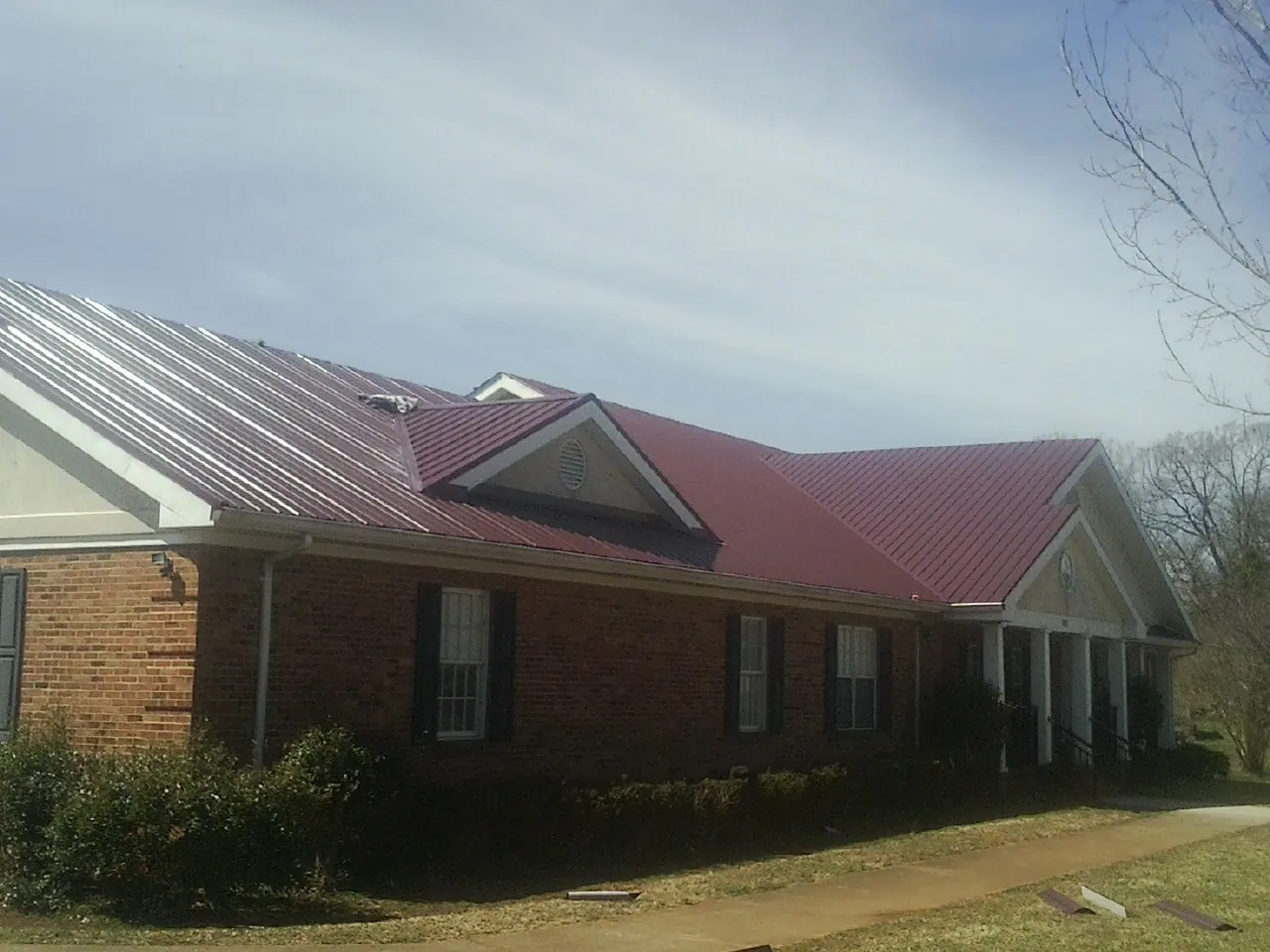 Red metal roof with gabled entries on a long brick building, from a Hail Damage Roof Repair job in Chualar