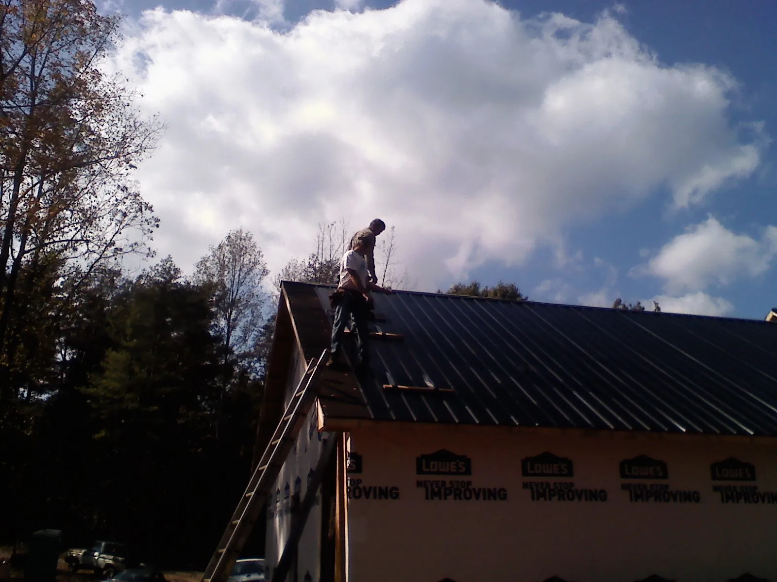 Roofer fastening dark metal panels high against a cloudy sky, from a Roof Inspection job in Chualar