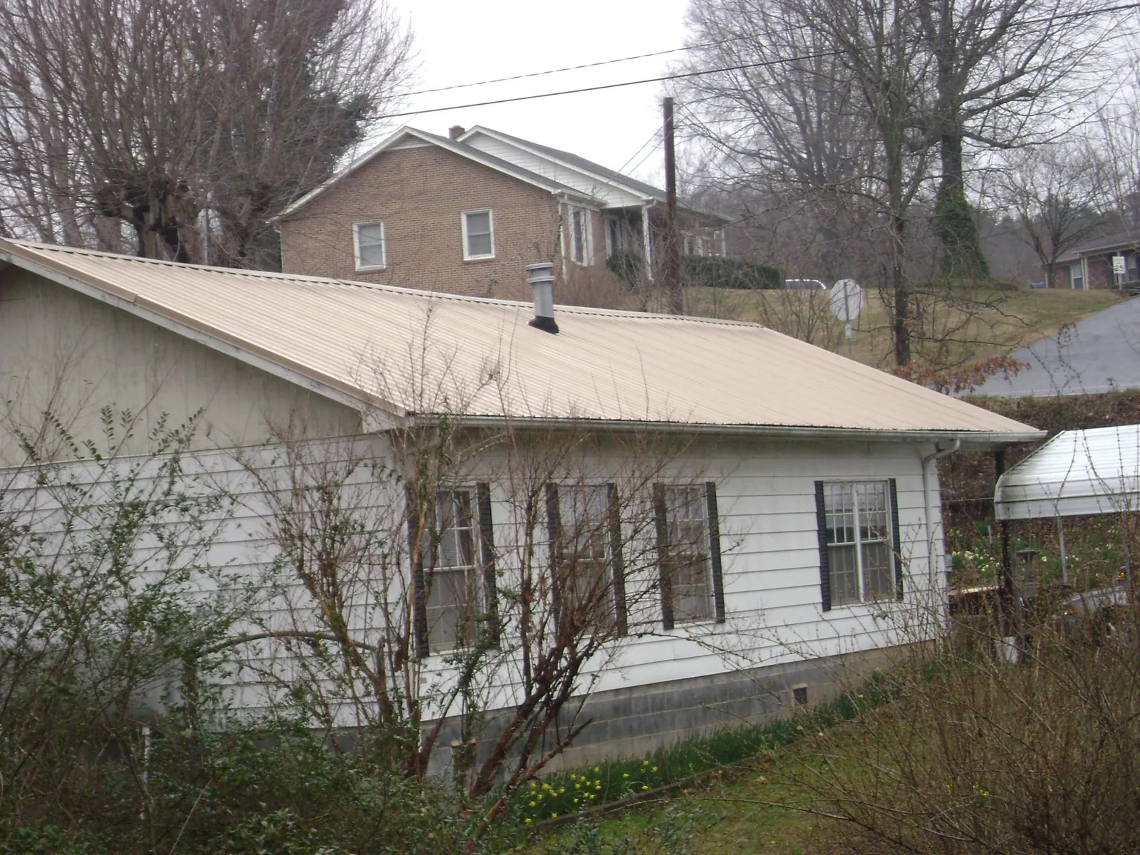Tan metal roof on a white sided house set into a hillside — Commercial Roofing by Roofing Brothers in Chualar